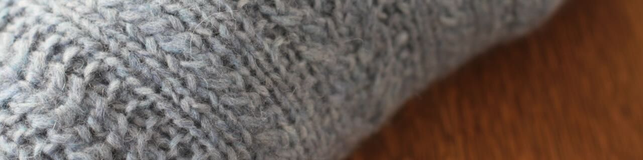 Close-up detail of a light blue cabled sweater folded on a wooden table.